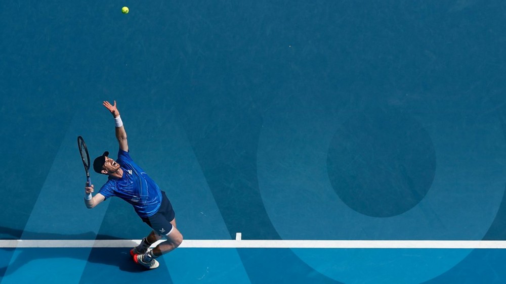 一名男子网球运动员站在底线发球。 他在澳大利亚网球公开赛上，他们正在那里投放新的 2023 NFT。