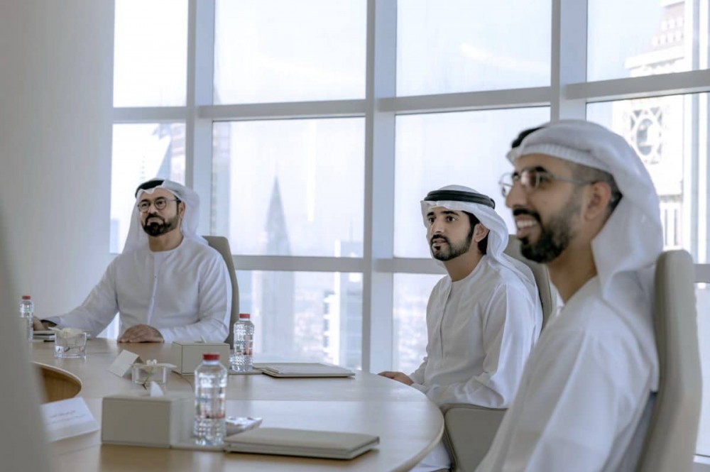 三名身着白衣的男子坐在圆桌旁，支持谢赫哈姆丹的 100 天计划。