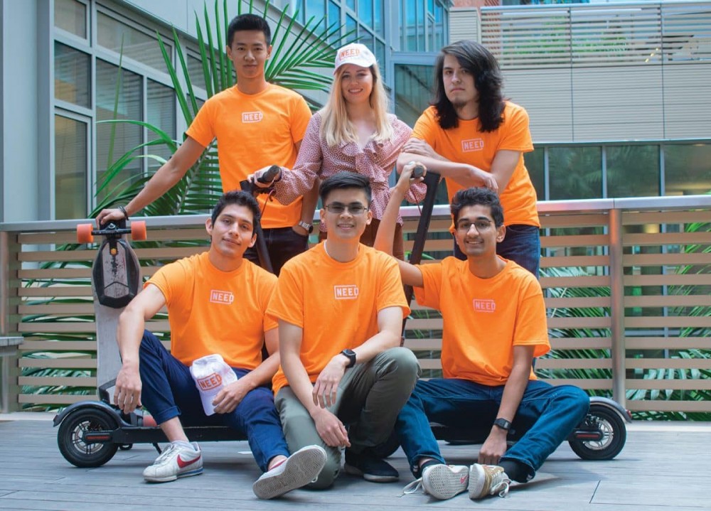 六名身穿亮橙色衬衫的大学生在一辆电动滑板车前坐着站着。 其中之一是 Frank DeGods，他刚刚对自己进行了 doxxed。