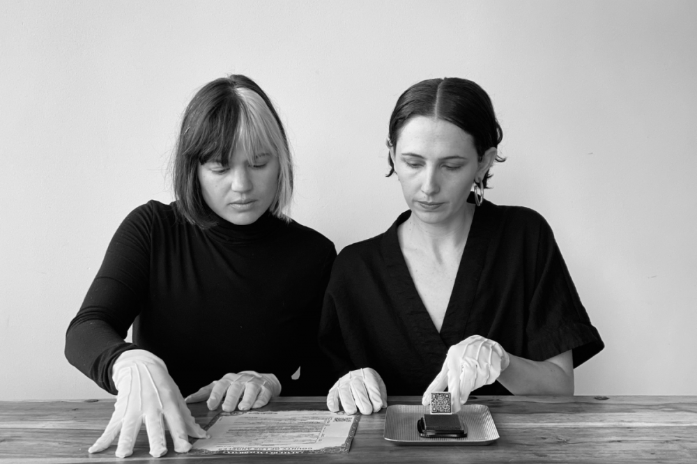 一张黑白照片，两个女人坐在桌旁，戴着白手套，正在签结婚证。
